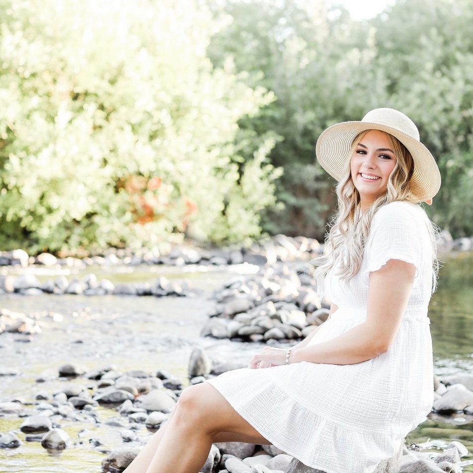 senior photo outfit ideas with girl sitting on a rock next to a river in a white dress 