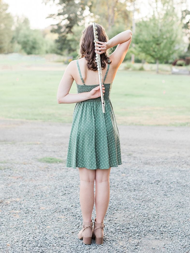 senior photos of girl in a green sun dress holding her flute while standing outside for her senior session