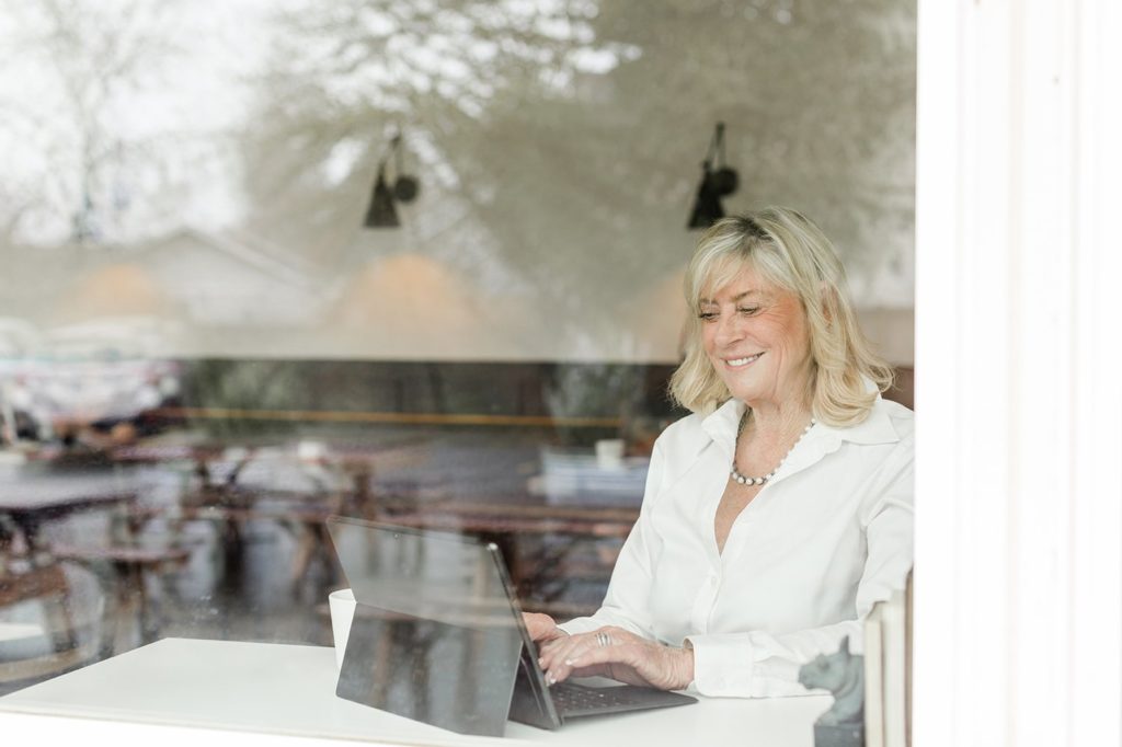 woman sitting at a table in a window working on her computer while smiling for Eugene Oregon brand photos