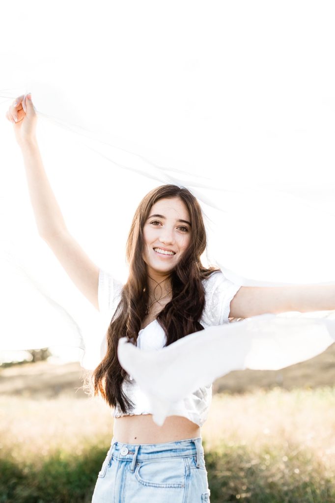Eugene Oregon senior session with girl smiling in a field holding white scarf backlit