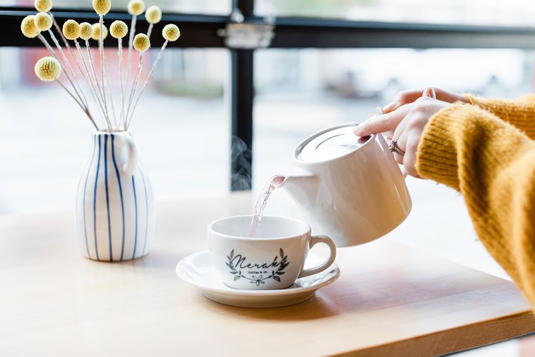 Oregon branding photographer captures tea being poured into teacup from ceramic tea pot yellow sweater yellow flowers in striped blue vase