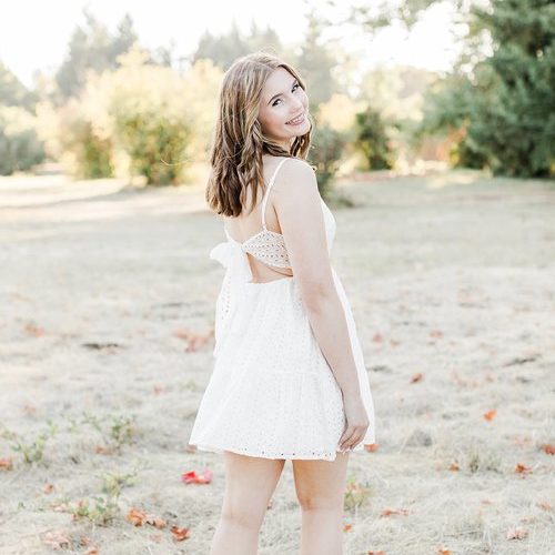 senior pictures with girl walking away from the camera in a field in Oregon while she wears a white dress