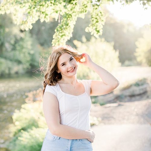 high school senior in jeans and a white shirt stands on a path under a tree in Eugene for her senior year photos