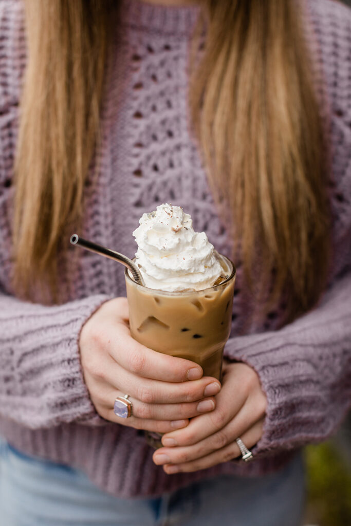 woman holding iced coffee with whipped cream with metal straw