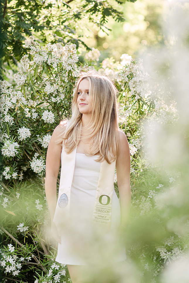 Girl looking to the side with Oregon graduation stole around neck with green plant in background